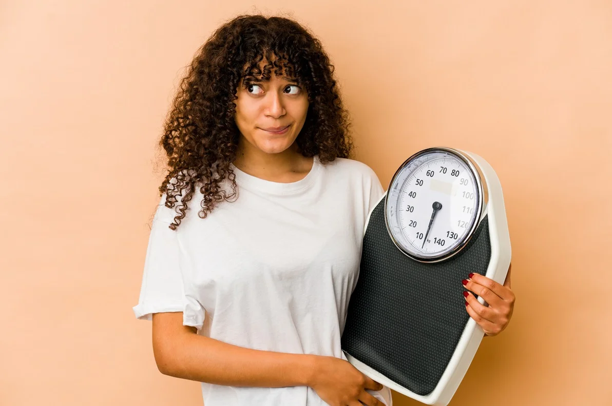 A woman holding a scale, contemplating weight, symbolizing the importance of weight management for effective rucking.